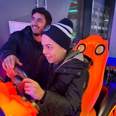 A child playing a racing car game with a carer in an arcade.